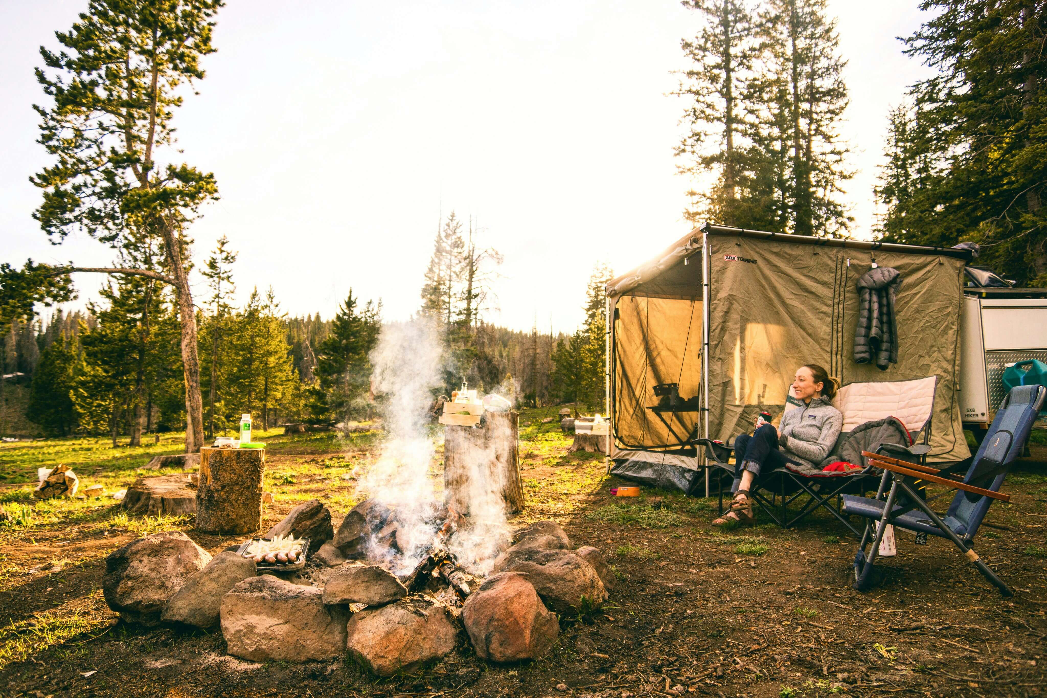 someone sitting in a chair by a fire at her campsite