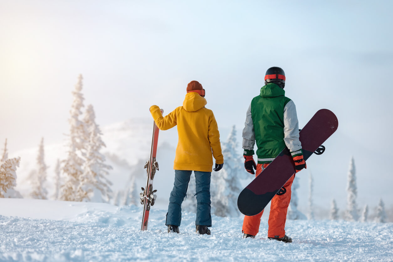 a skiier and a snowboarder standing at the top of a snowy hill