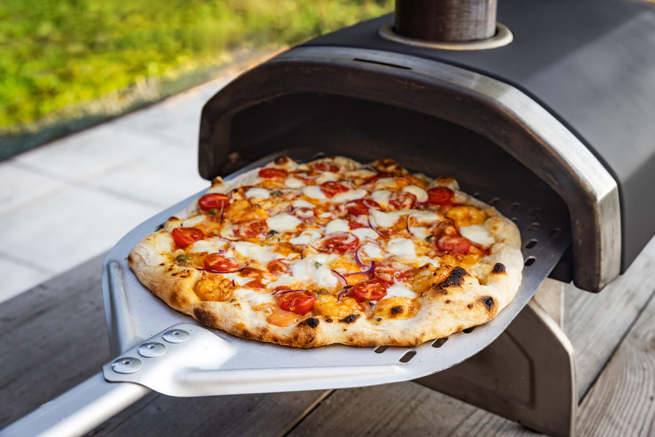 someone cooking a pizza in a pizza oven at a backyard party